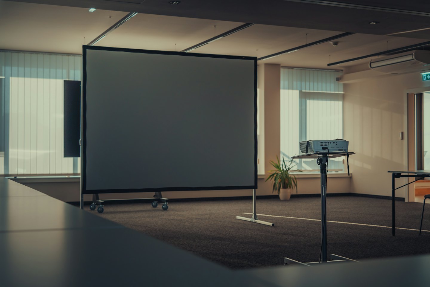 Pusta sala konferencyjna z przygotowanym ekranem projekcyjnym i projektorem.