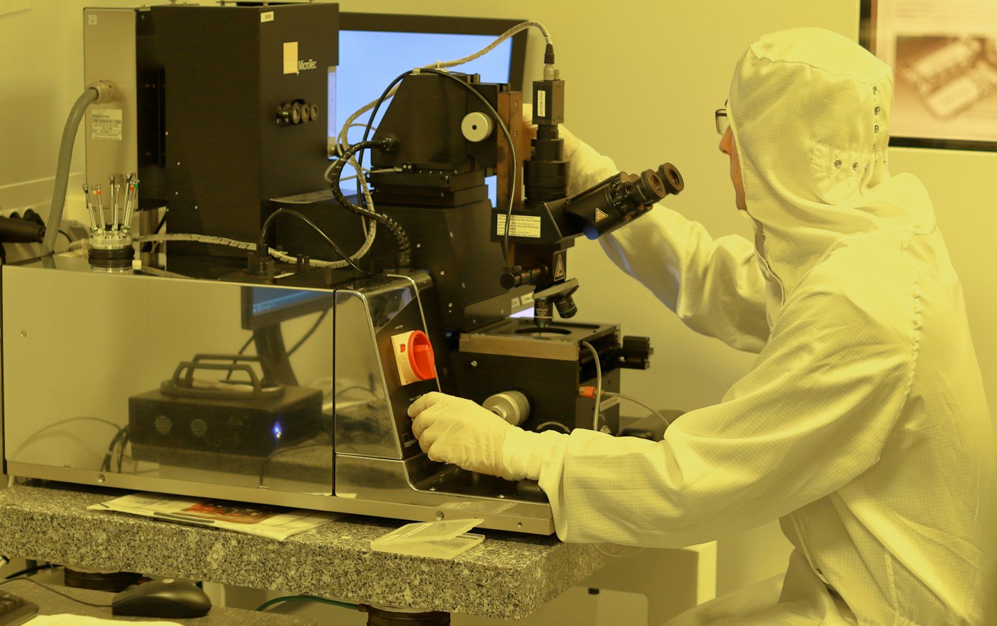 Naukowiec w kombinezonie laboratoryjnym obsługuje skomplikowany instrument z mikroskopem.